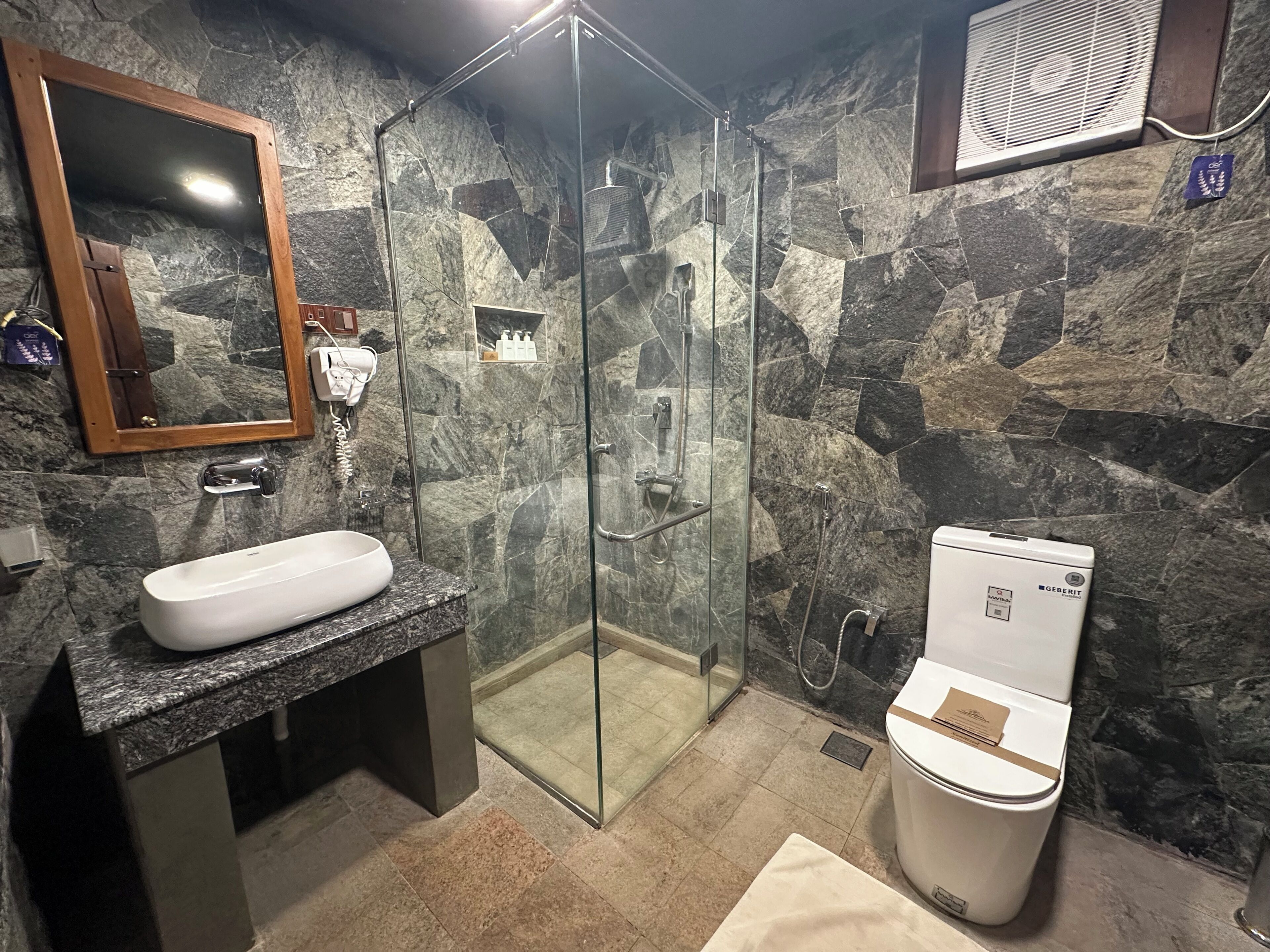 Un baño con pared de piedra, cabina de ducha de vidrio, lavabo e inodoro.