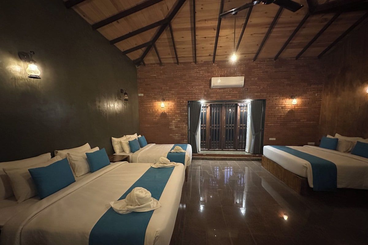 Habitación de hotel con cuatro camas, pared de ladrillo, vigas de madera y puerta corrediza de vidrio.