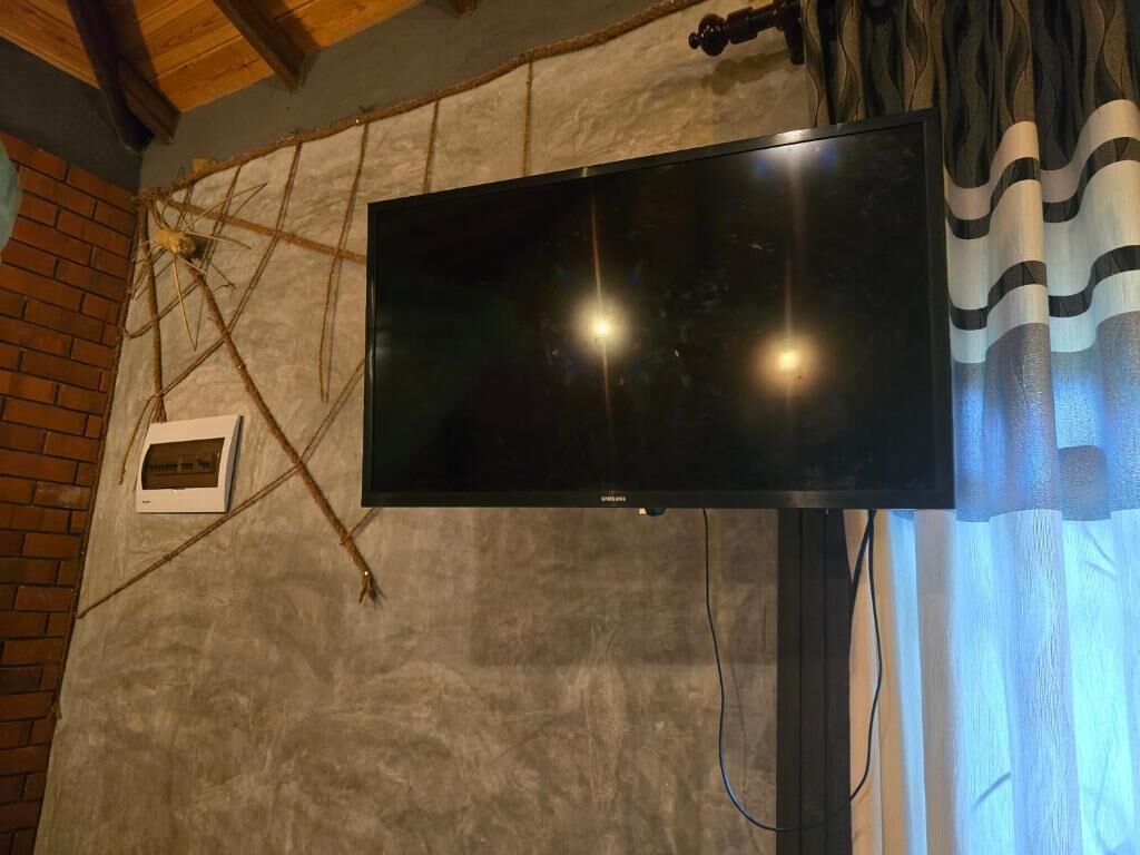 Een flatscreen televisie bevestigd aan een structuurrijke muur met zichtbaar baksteen en een raam met gordijnen.