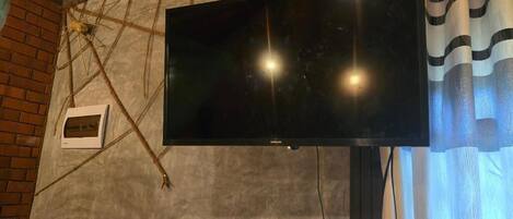 Een flatscreen televisie bevestigd aan een structuurrijke muur met zichtbaar baksteen en een raam met gordijnen.