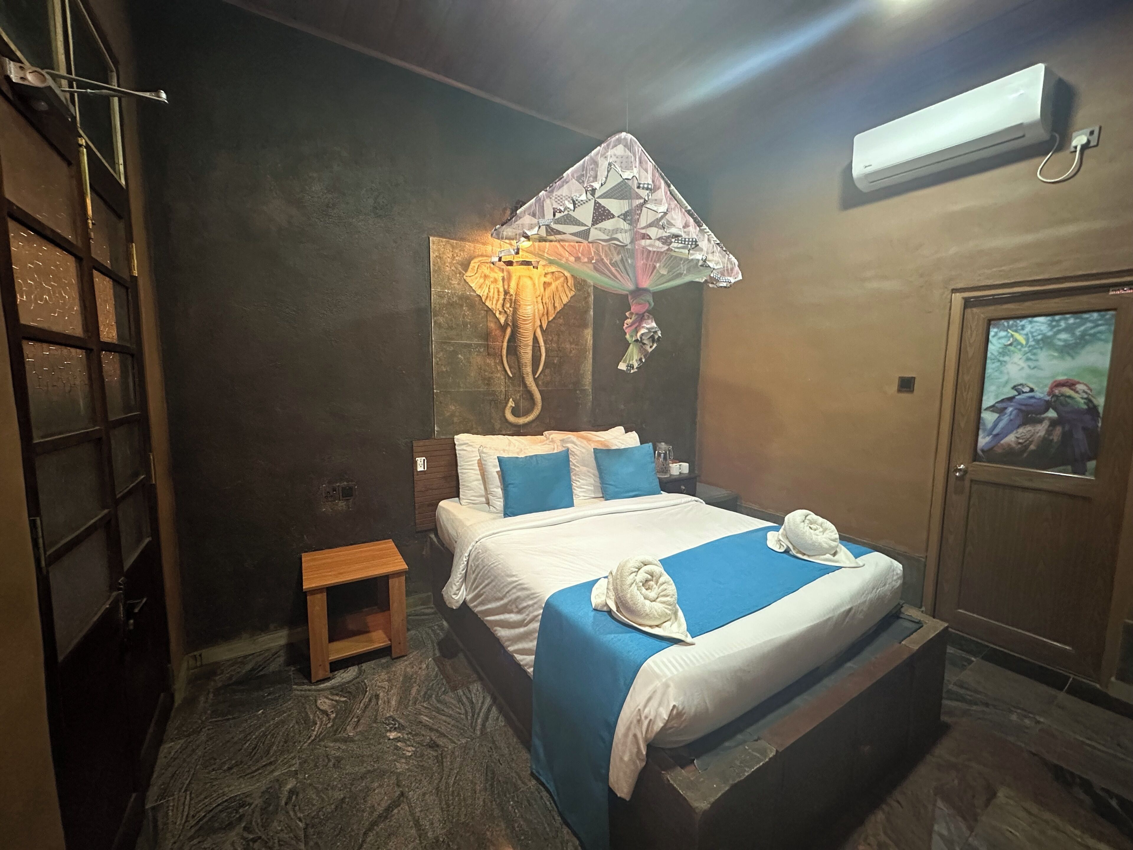 A bedroom with a bed, a nightstand, a small table, a wall-mounted air conditioner, and a door with a window.