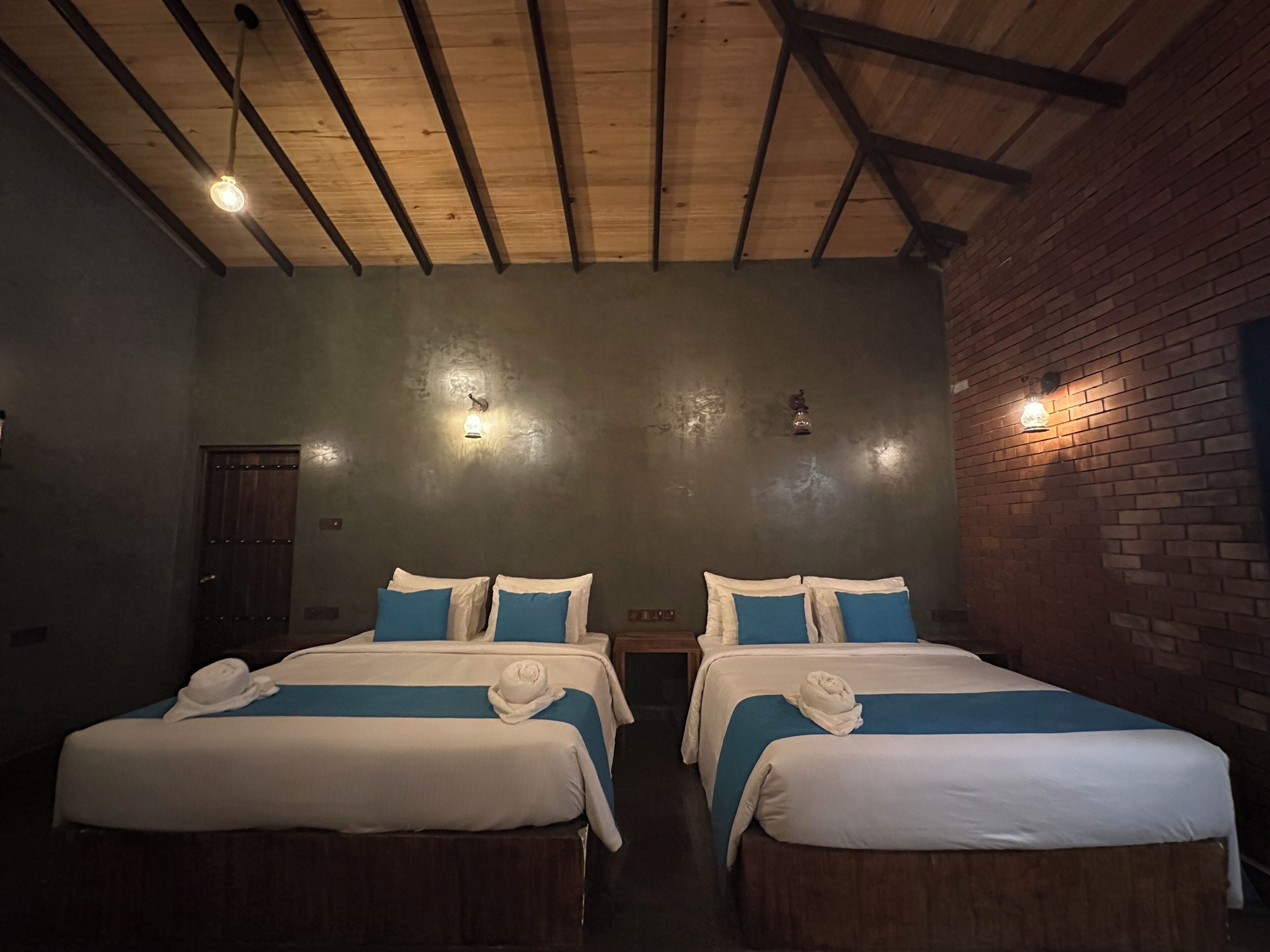 Une chambre avec deux lits, chacun recouvert d’une courtepointe bleue et blanche, dotés de têtes de lit en bois et bordée d’un mur en briques.