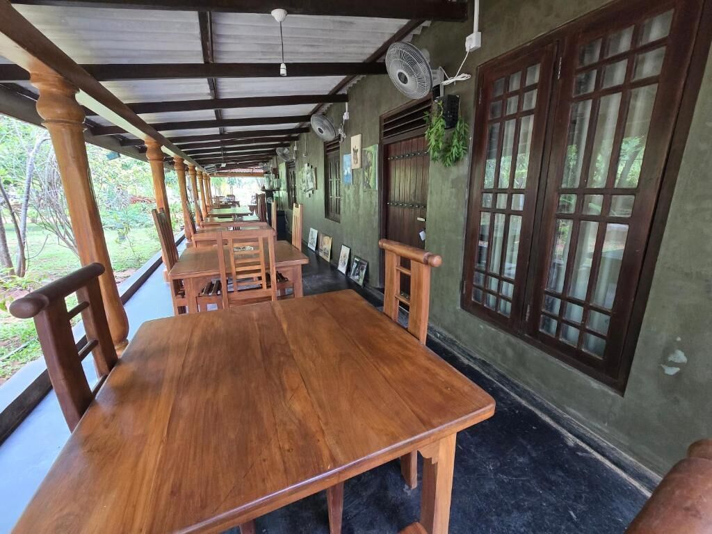 A covered outdoor dining area with wooden tables and chairs, large windows, and fans.