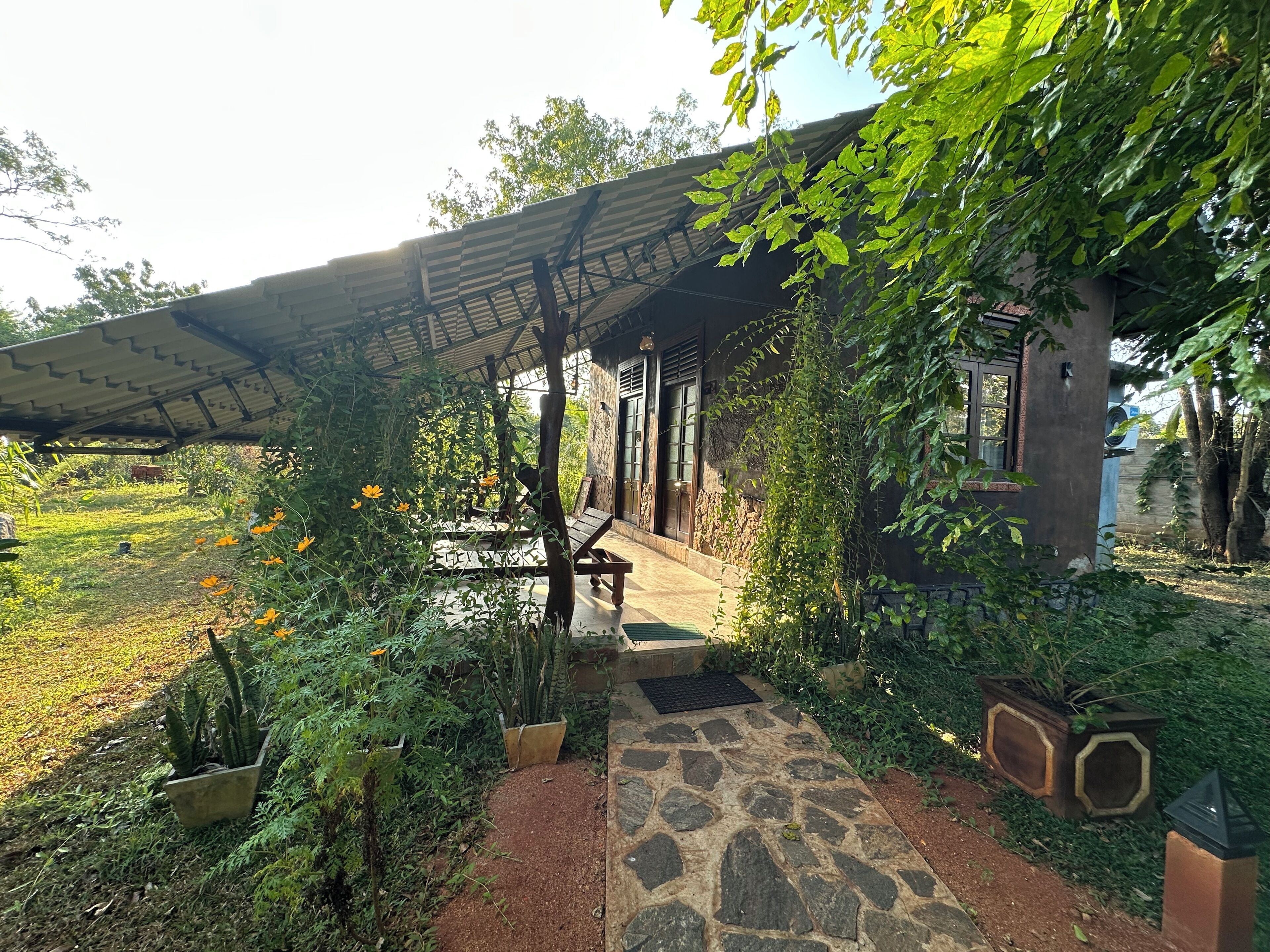 Un espacio de estar al aire libre cubierto con senderos de piedra, plantas en macetas y un edificio rústico.