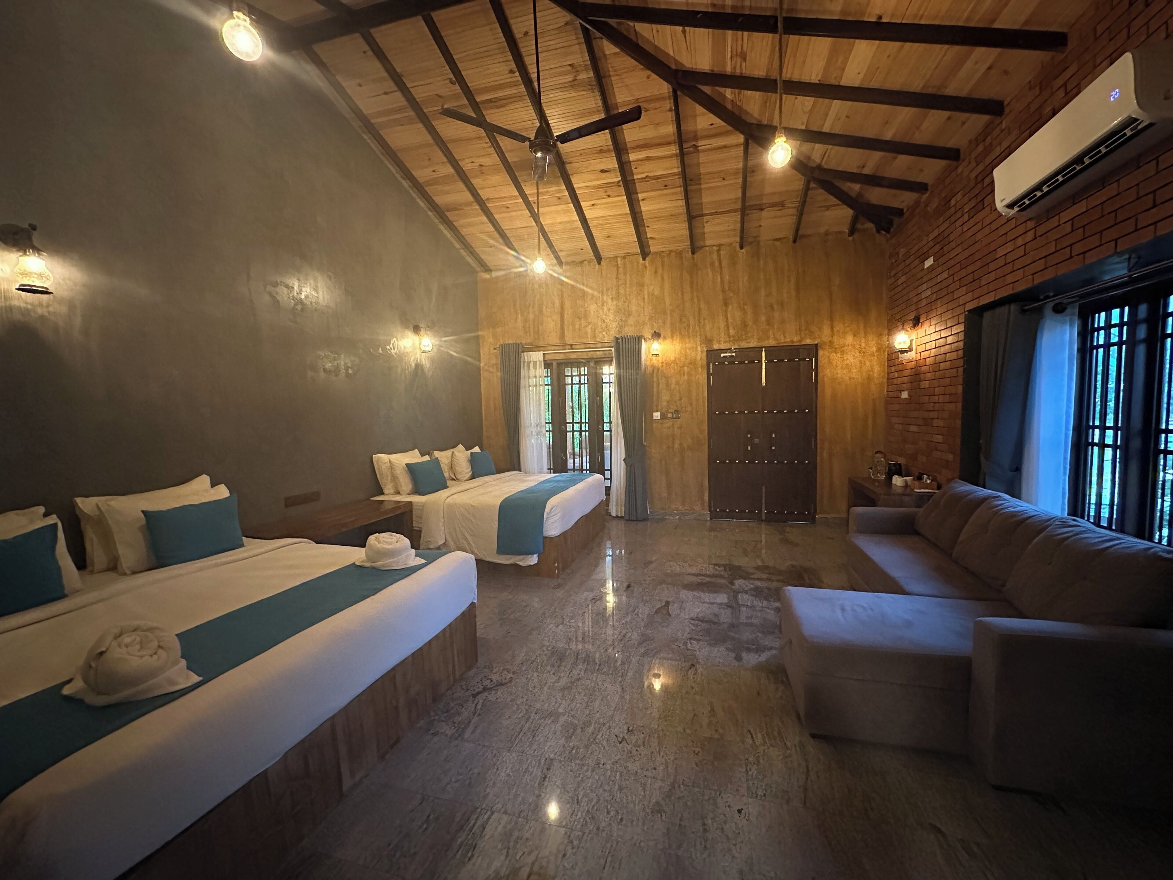 A hotel room with two beds, a sofa, a ceiling fan, an air conditioning unit, and a view of the outdoors.