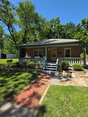 A brick house with a front porch, a front door, and a small garden area.