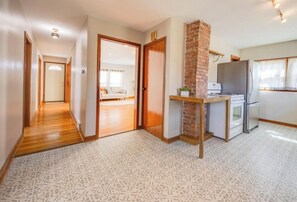 A hotel room with a patterned floor, a kitchen area with a refrigerator, stove, and microwave, a brick accent wall, and a hallway leading to another room.