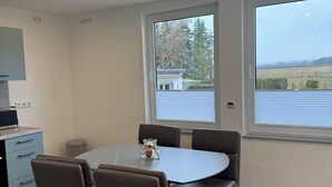 Ein Essbereich mit einem runden Tisch, vier Stühlen und einem Fenster mit Blick auf ein Gebäude und Bäume.