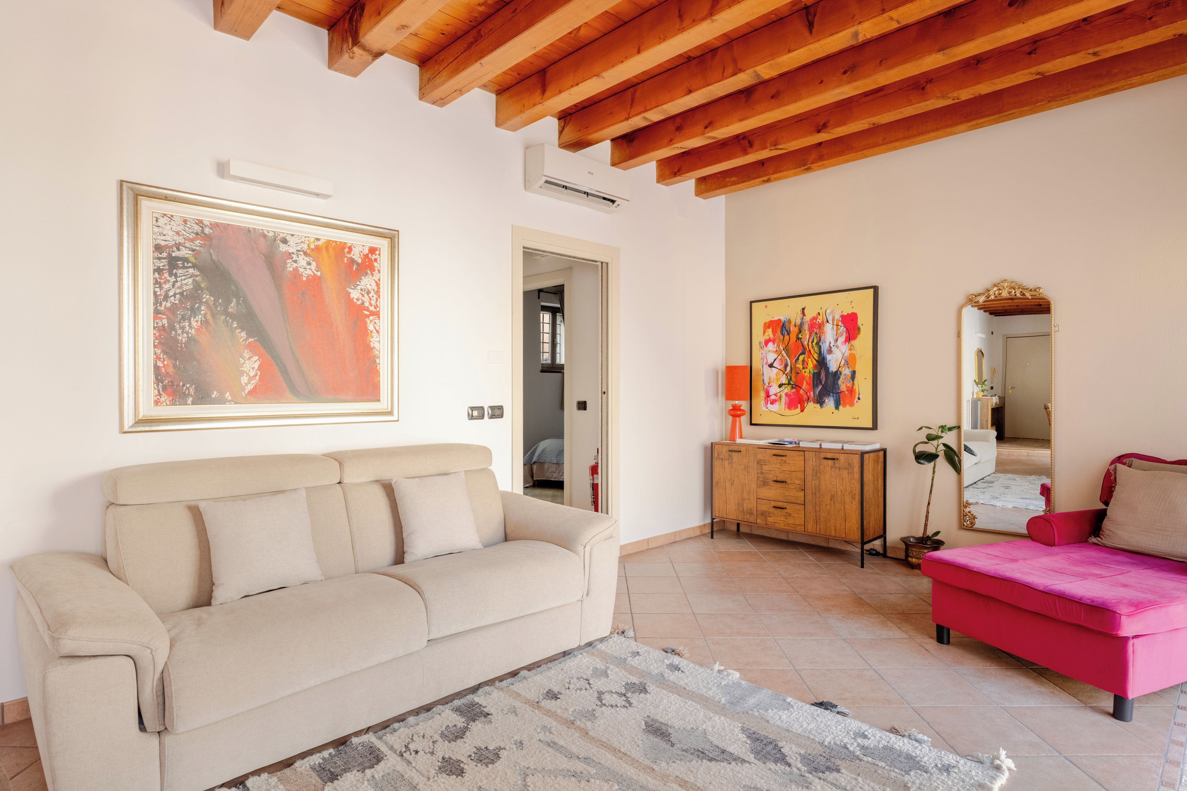 Un soggiorno con un divano beige, un divano rosa, un armadio in legno e due quadri alle pareti.