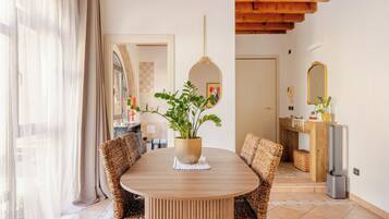 A dining area with a round wooden table, wicker chairs, a potted plant, and a mirror on the wall.