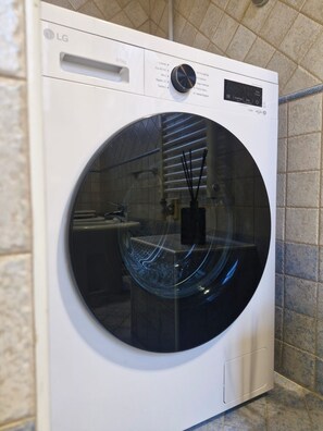 Un lave-linge LG à chargement frontal, situé dans une salle de bain dont les murs sont recouverts de carreaux et où l’on peut voir un lavabo.