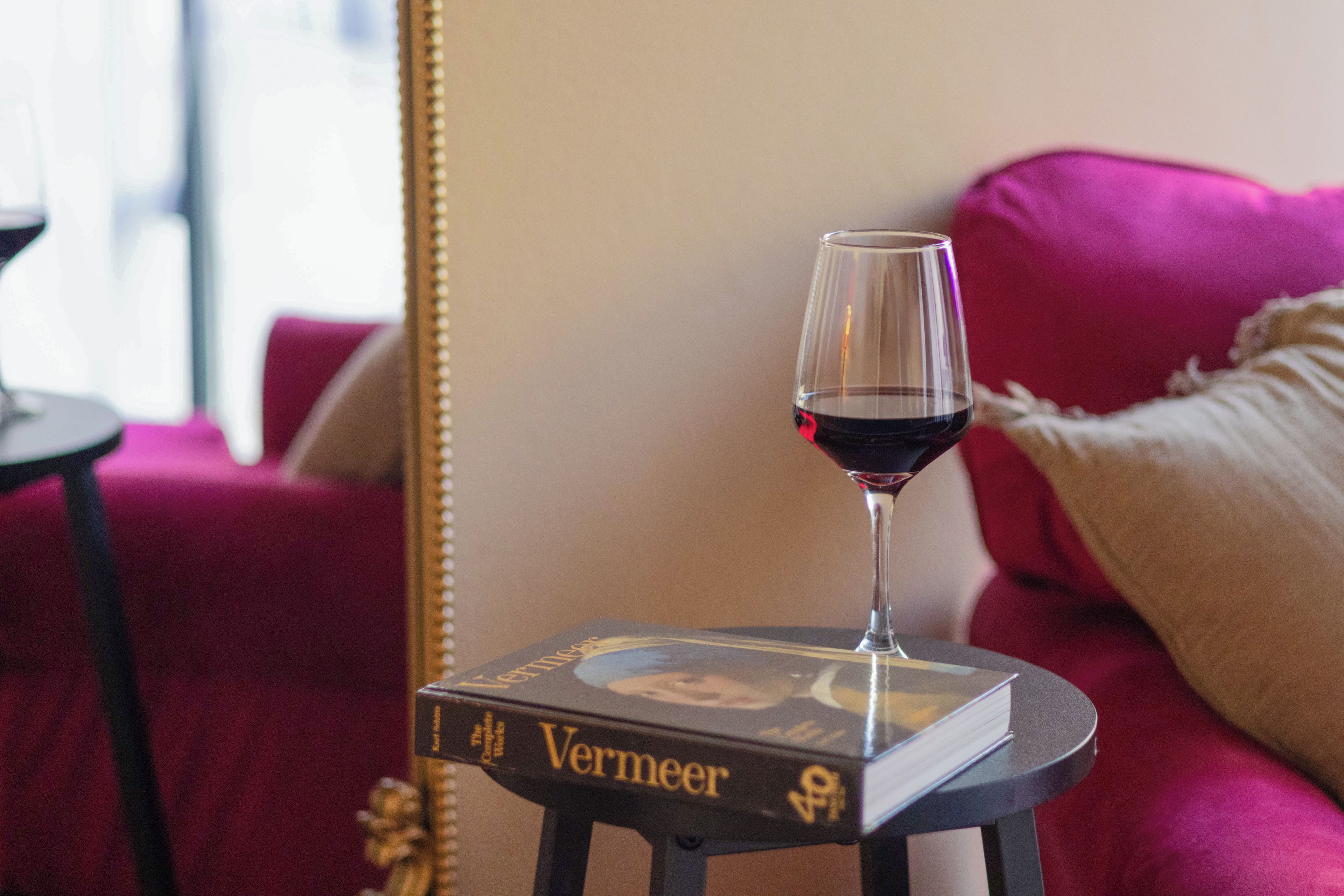 Ein Buch mit dem Titel 'Vermeer' auf einem kleinen Tisch zusammen mit einem Glas Rotwein.