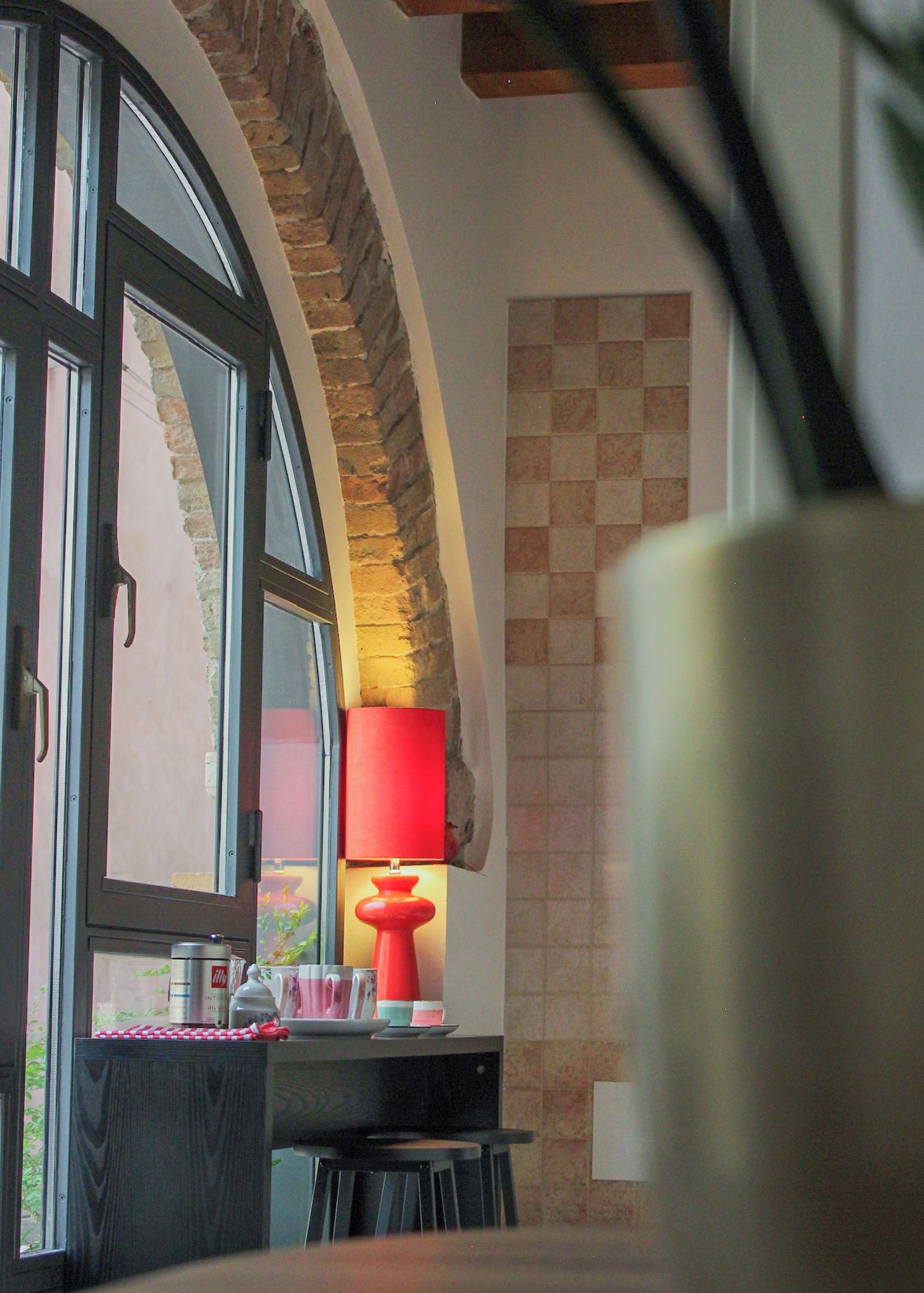 A room with a table, chairs, a lamp, and a window with a view of a brick wall.
