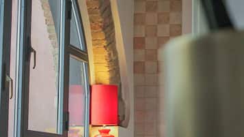 A room with a table, chairs, a lamp, and a window with a view of a brick wall.