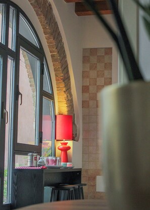 A room with a table, chairs, a lamp, and a window with a view of a brick wall. - [Free Parking] - 7 Min from Juliet's | 4 Guests (Verona)