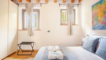 Una camera da letto con un letto, un tavolino, due finestre con tende e un quadro appeso al muro.