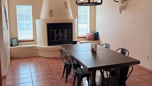 Uma sala de jantar com uma mesa e cadeiras de madeira, lareira e teto com vigas aparentes.