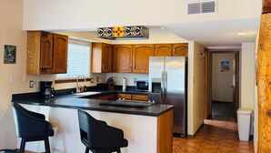 Uma cozinha moderna com vigas de madeira, uma ilha central, banquetas pretas e eletrodomésticos de aço inoxidável.