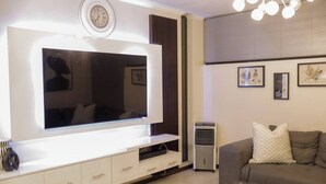 A modern living room with a flat-screen TV, a sofa, a coffee table, and a wall-mounted clock. - Luxurious, Spacious 2-br (Johannesburg)