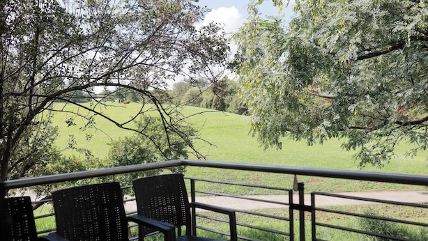 A balcony with chairs overlooking a grassy field and trees. - Luxurious, Spacious 2-br (Johannesburg)
