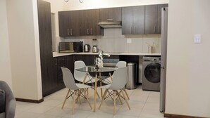 A modern kitchen with dark wood cabinets, a stainless steel refrigerator, a built-in oven, and a washing machine. - Luxurious, Spacious 2-br (Johannesburg)