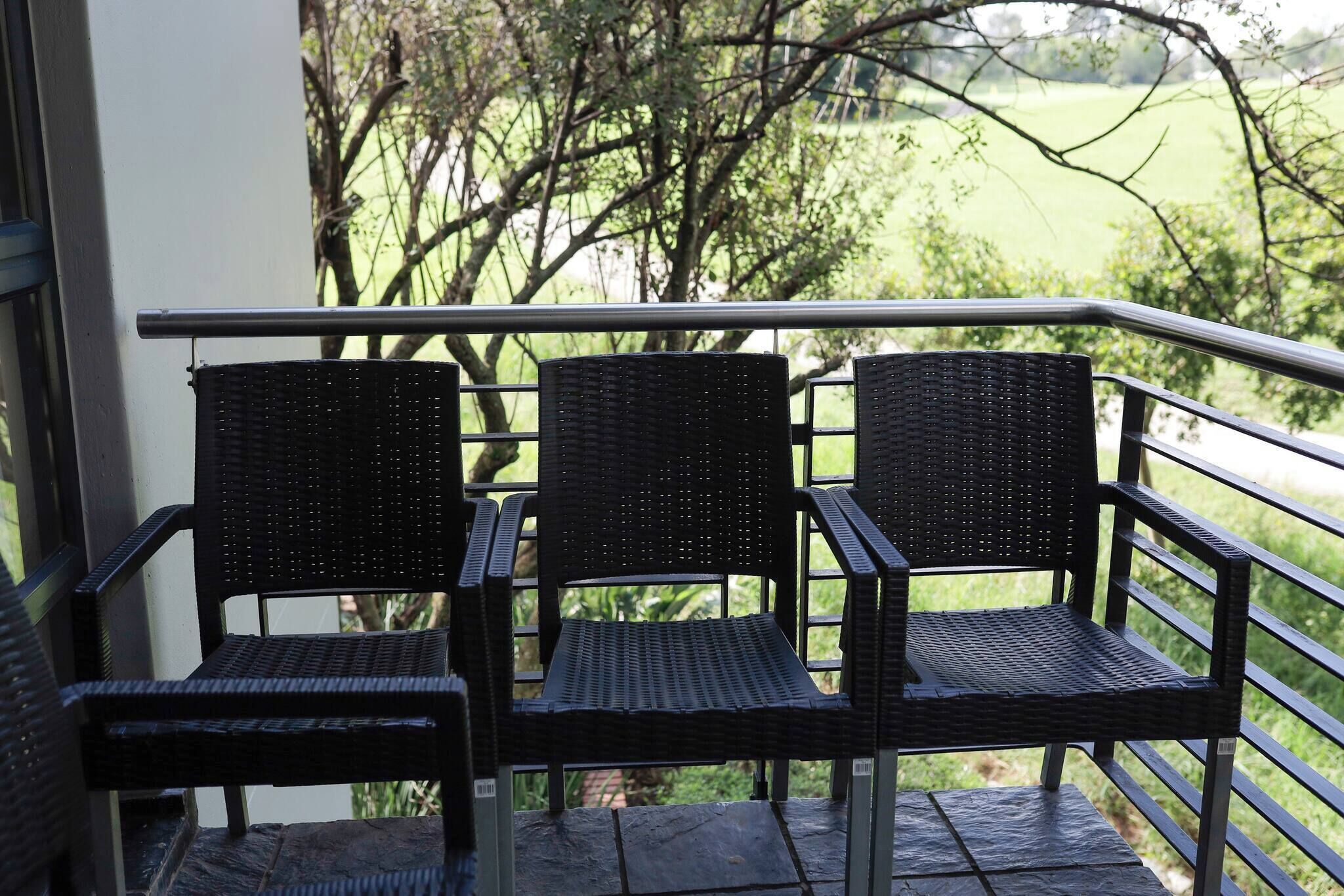 Three wicker chairs on a balcony with a metal railing, overlooking a green landscape.