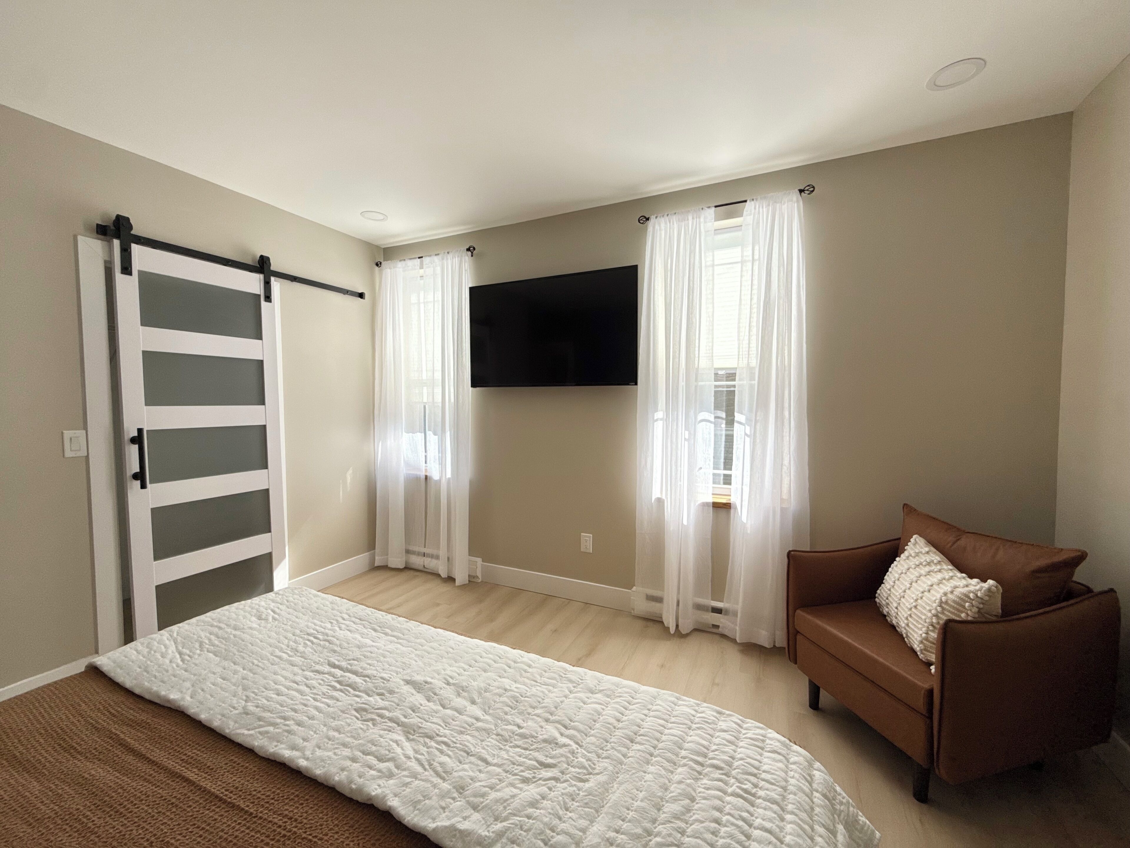 A bedroom with a bed, a brown sofa, a TV mounted on the wall, and a sliding door.