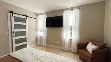 A bedroom with a bed, a brown sofa, a TV mounted on the wall, and a sliding door.