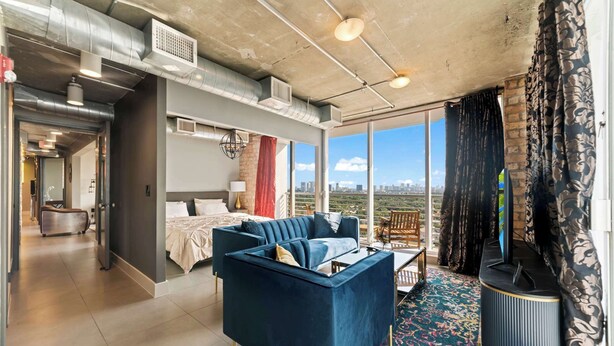 Ein modernes Wohnzimmer mit einer Couch, einem Fernseher und einem großen Fenster mit Blick auf die Stadt.