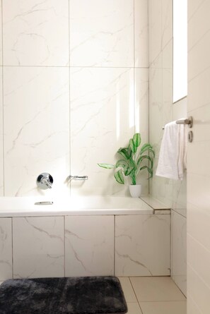 Ein Badezimmer mit Marmorwand, einer weißen Badewanne, einer Topfpflanze und einem Handtuchhalter.