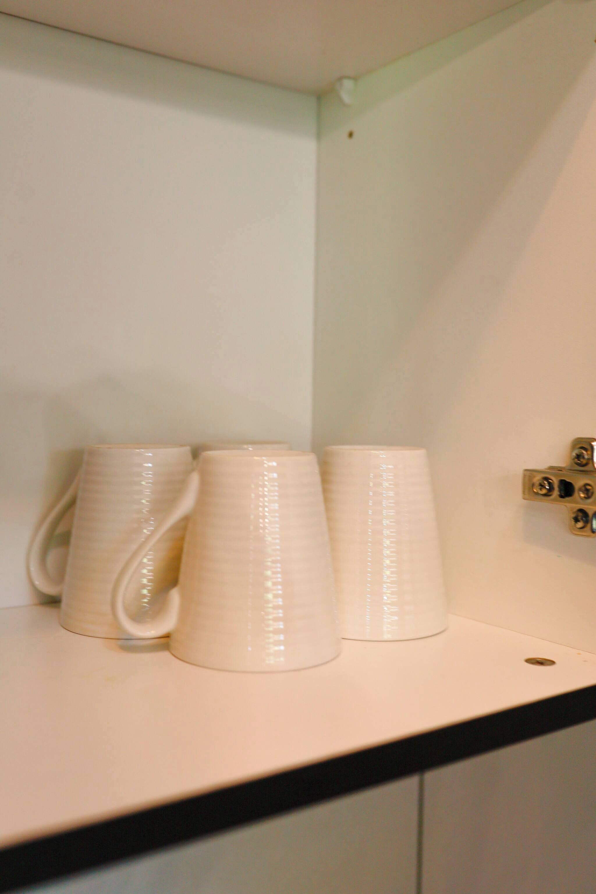 Tres tazas de cerámica blanca sobre un estante blanco en un rincón de la habitación.