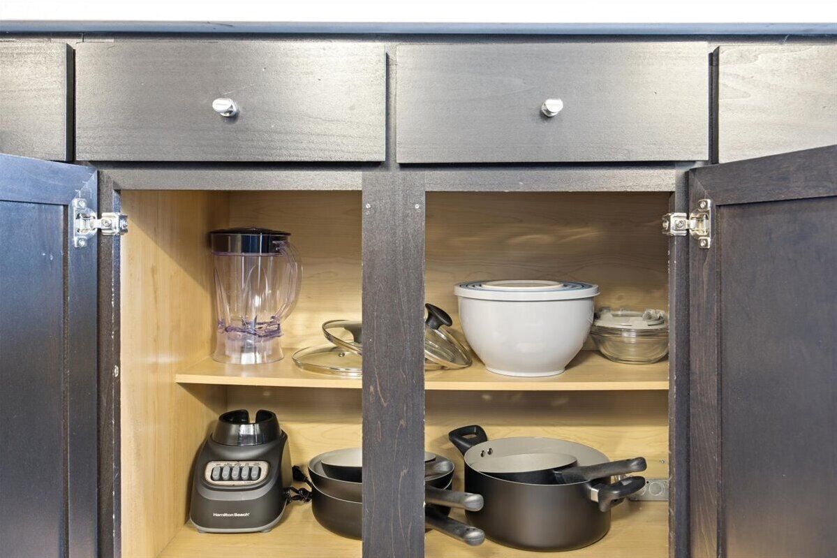 A kitchen cabinet with two drawers and a shelf, containing a blender, pots, and a glass container.