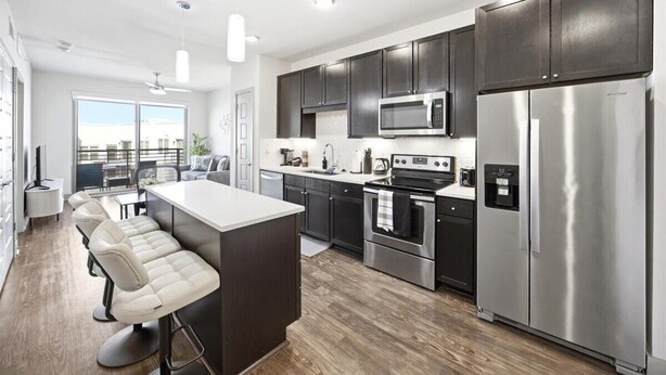 A modern kitchen with dark cabinets, stainless steel appliances, and a bar area with stools. - Modern Oasis + Pool, Gym + EV Charger (Frisco)