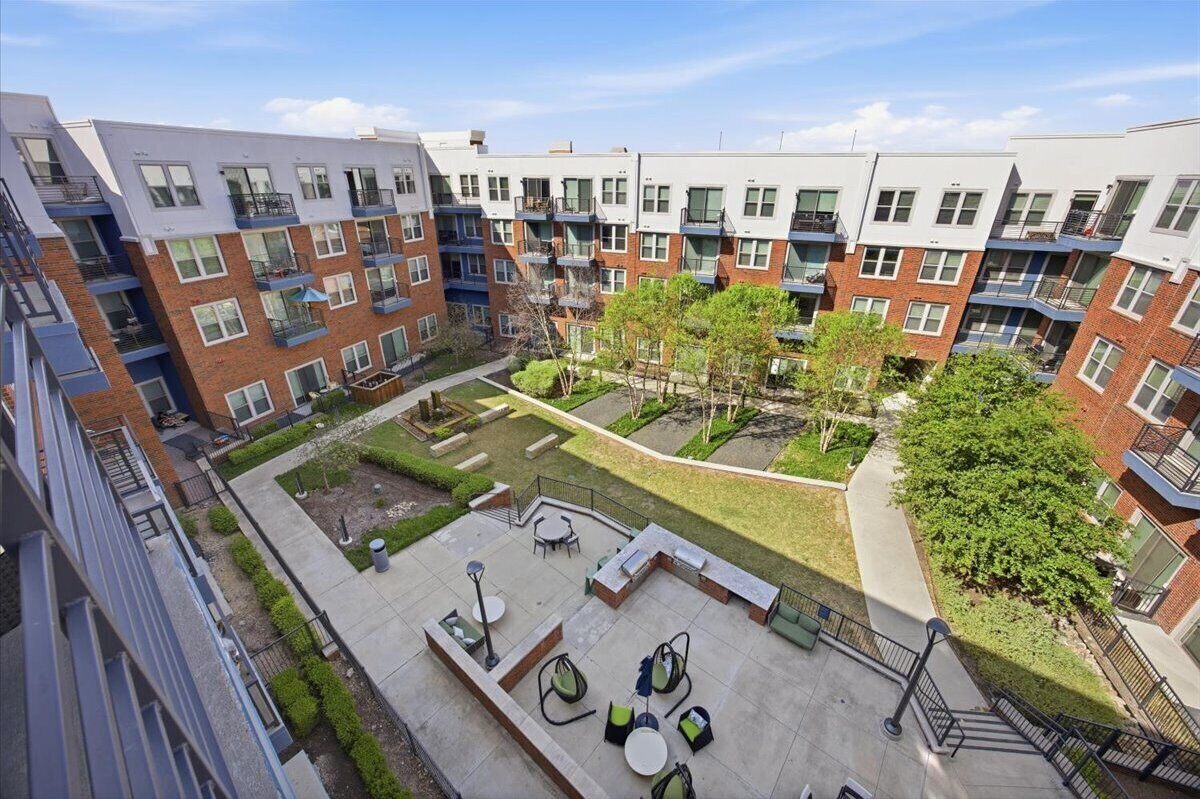 A multi-story residential building with balconies, a courtyard with seating, and a small garden area.