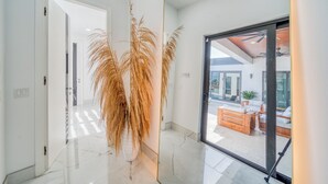 A modern interior with a hallway leading to a glass door, a potted plant, and a view of an outdoor seating area. - Cozy Modern Villa - Heated Pool & Spa - BBQ - Water View (Cape Coral)