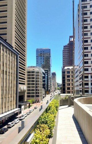A city street lined with modern buildings, a clear sky, and a sidewalk with greenery. - Stylish 1 BR Getaway, Fast Wi-fi, Beach Access (Cape Town)
