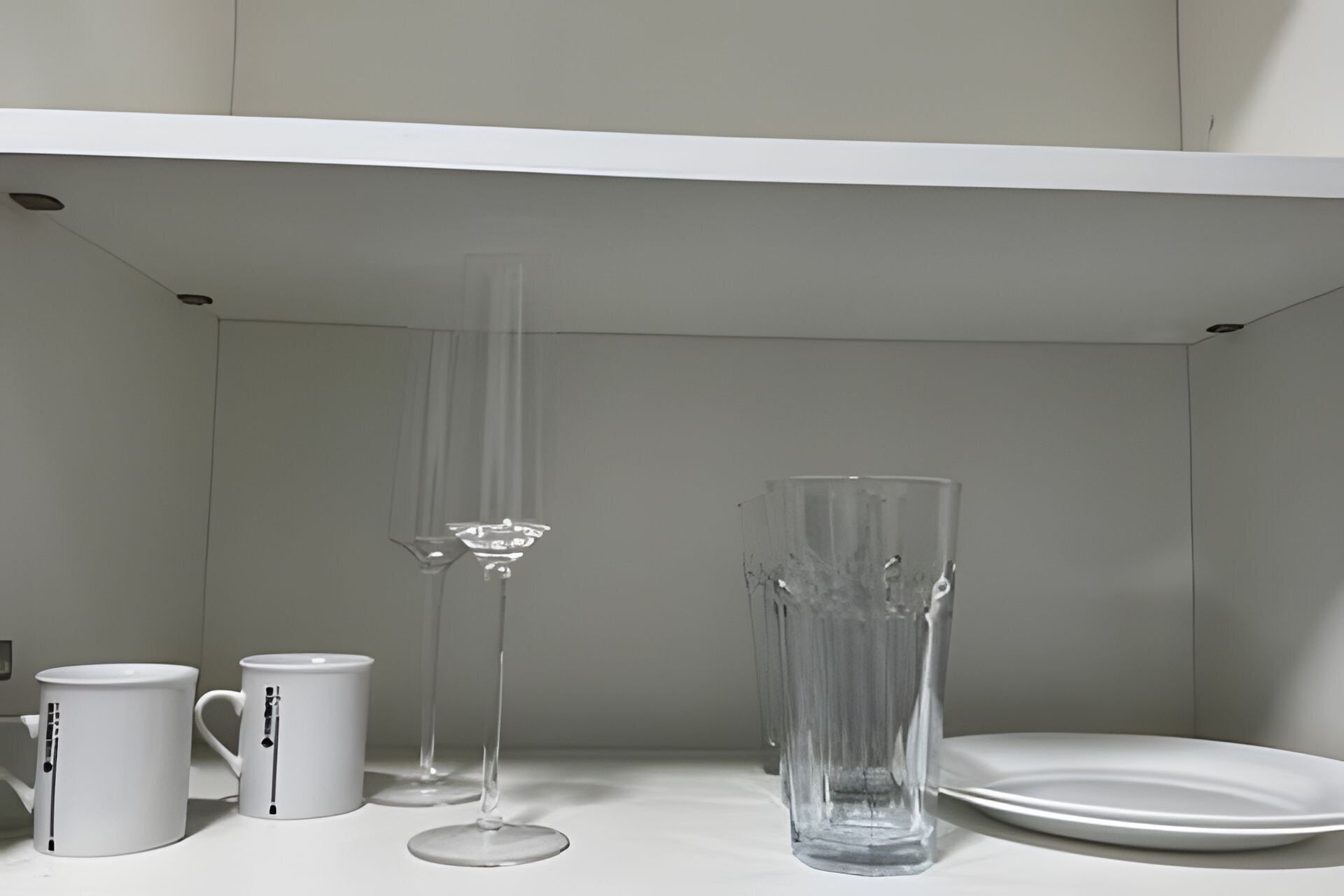 A white shelf with three clear glassware items and two white mugs with black designs.