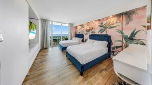 Et hotelværelse med to senge, et stort vindue med udsigt og et vægmaleri med tropisk tema.