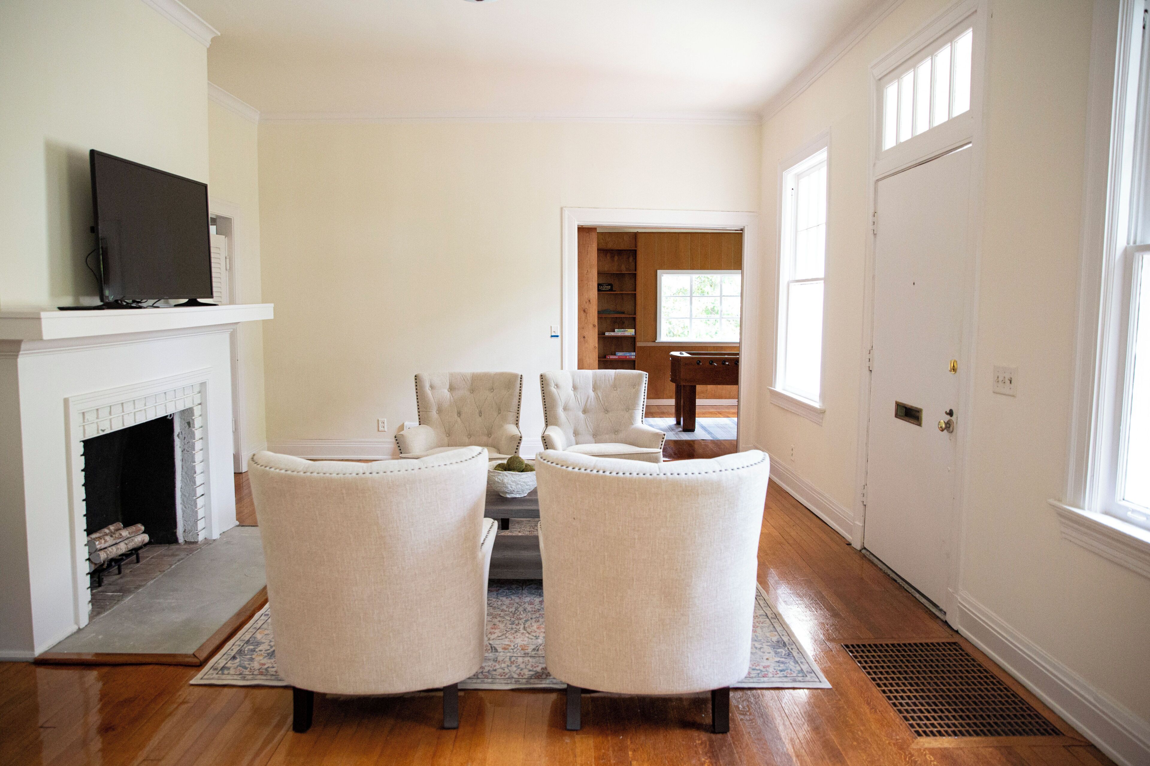 Un salon avec une cheminée, deux fauteuils, une table basse et un téléviseur posé sur un meuble.