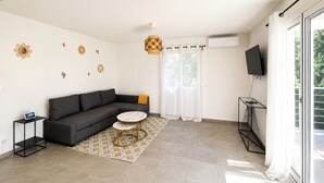 Un salon moderne avec un canapé, une petite table ronde, un téléviseur et une grande fenêtre.