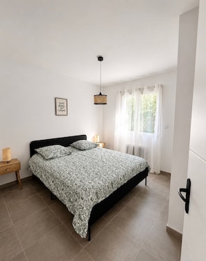 A bedroom with a bed, a bedside table, a hanging light fixture, a window with curtains, and a wall-mounted radiator. - New house with private pool (Ruoms)