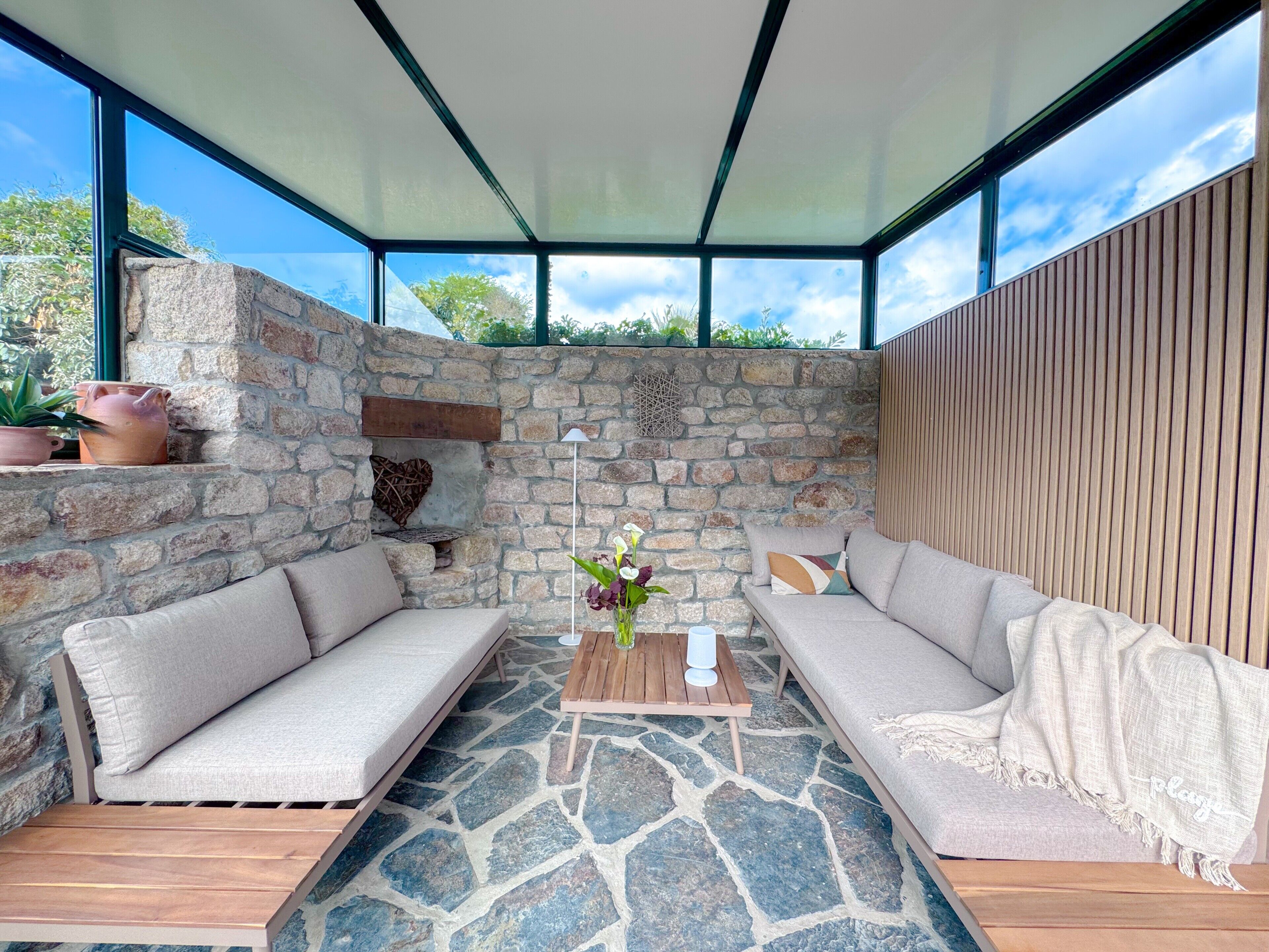 A modern outdoor seating area with stone walls, a wooden bench, and a cushioned sofa.