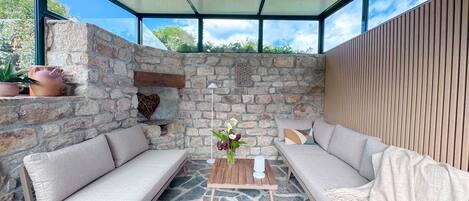 A modern outdoor seating area with stone walls, a wooden bench, and a cushioned sofa.