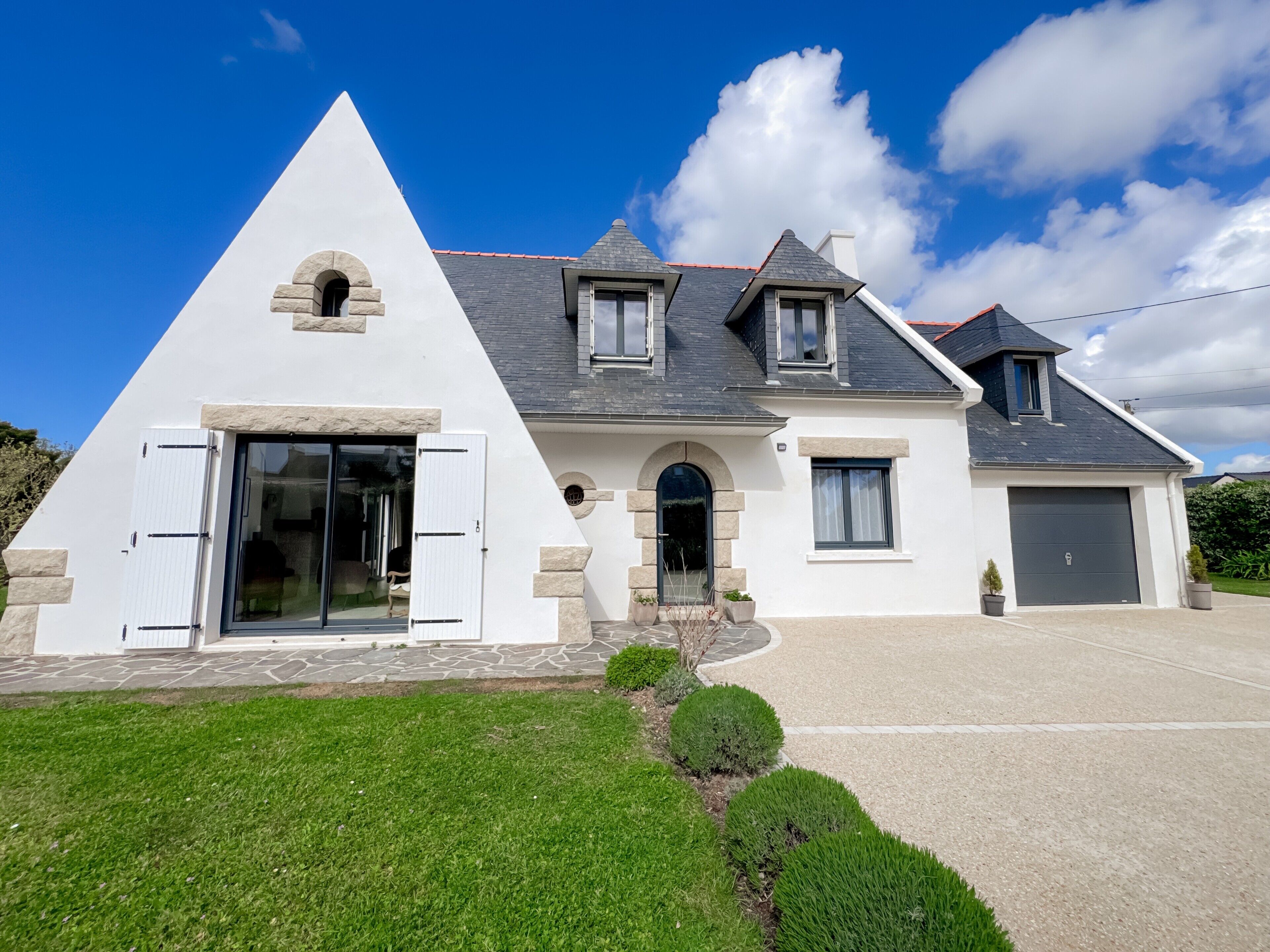 A modern house with a triangular front, a garage, and a well-maintained lawn.