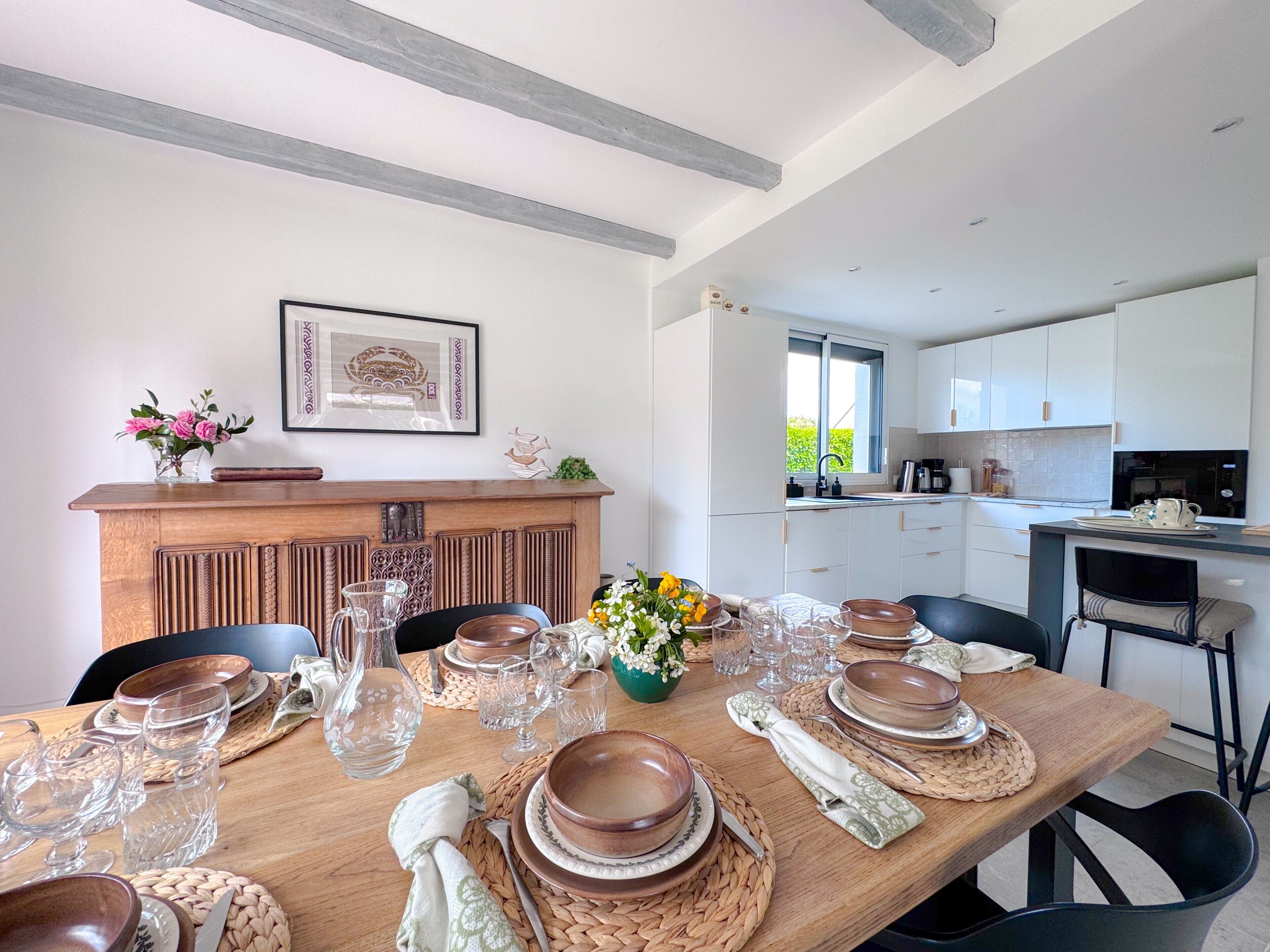 A modern kitchen with white cabinets, a wooden dining table set for four, and a kitchen island with a sink.