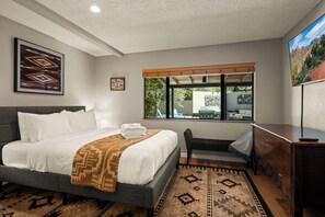 A hotel room with a bed, a desk, a chair, a window with a view, and a mounted artwork. - Sedona Wellness Retreat: Gym + Sauna + Steam + Tub (Sedona)
