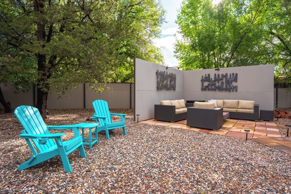 An outdoor seating area with Adirondack chairs and a sofa, surrounded by a gravel patio and trees. - Sedona Wellness Retreat: Gym + Sauna + Steam + Tub (Sedona)