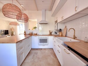 A modern kitchen with white cabinetry, a central island, and a large sink with a gold faucet. - Holiday Home “Léchiagat” with Private Terrace and Wi-Fi (Treffiagat)