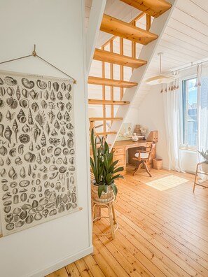 A room with a wooden floor, a desk, a chair, a potted plant, and a wall with a detailed illustration.