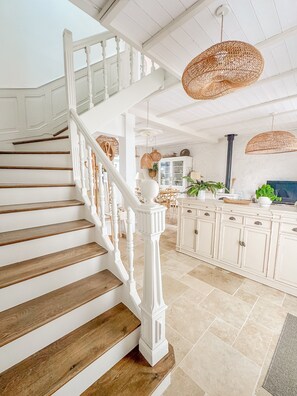A staircase with wooden steps and white railings, leading to a kitchen area with white cabinets and a dining table.